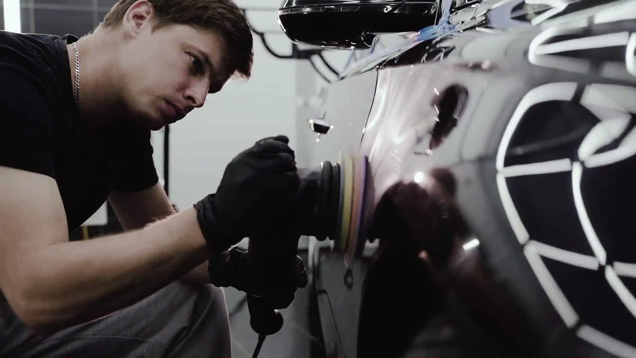 Technician carefully polishing the side of a black car